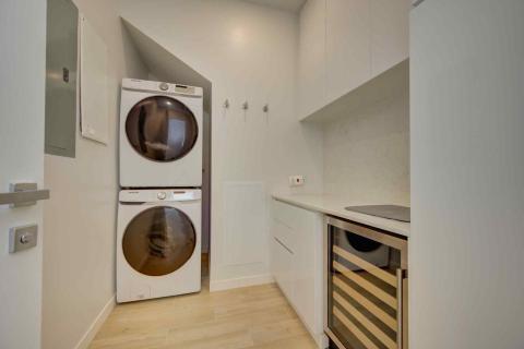 One Canal Point: Modern laundry room with stacked washer and dryer, counter space, and beige tiles  Title: One Canal Point: Modern laundry room with stacked washer and dryer, counter space, and beige tiles