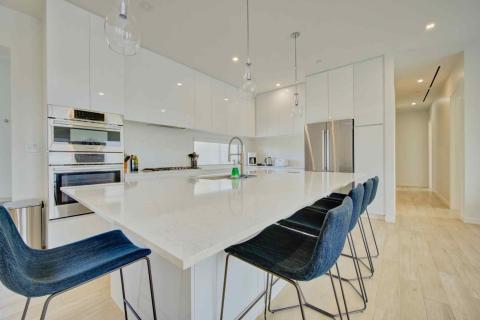 One Canal Point: Modern kitchen with white island, blue bar stools, and stainless steel appliances