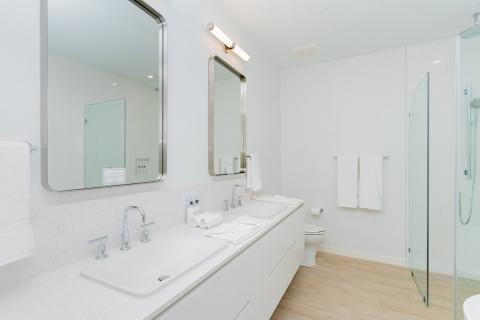 Modern bathroom with double sink vanity, glass shower, light wood-like tiles.