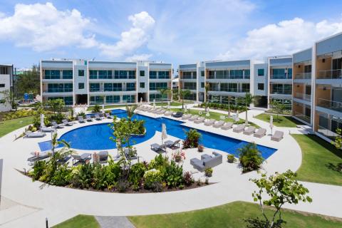 The image showcases a luxurious resort or apartment complex featuring a large, vibrant blue swimming pool at its center