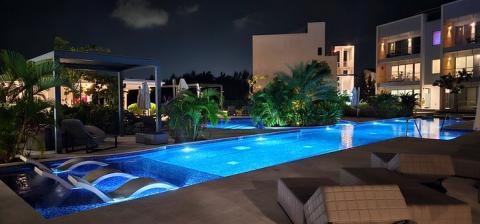 The image features a modern, luxurious outdoor setting at night, showcasing a beautifully illuminated swimming pool with a vivid blue hue