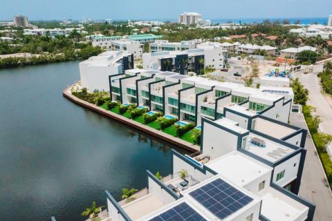 The image features a modern residential area located on the waterfront, showcasing several contemporary multi-story buildings with flat roofs