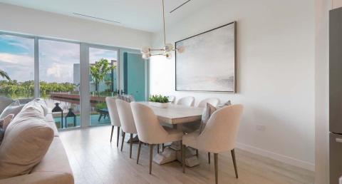 The image shows a modern, well-lit interior view of a living space overlooking an exterior water view through large sliding glass doors