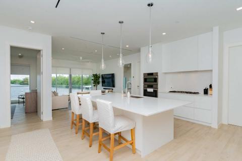 This image features a modern, bright kitchen and dining area looking out to a lake view through large glass sliding doors
