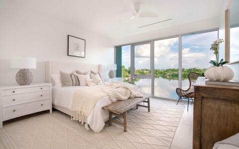 This image shows a beautifully decorated bedroom with a large window providing a scenic view of a calm lake surrounded by lush greenery