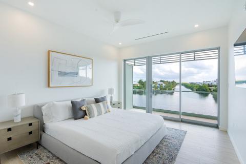 This image shows a modern and well-lit bedroom with a minimalist design, overlooking a scenic water view