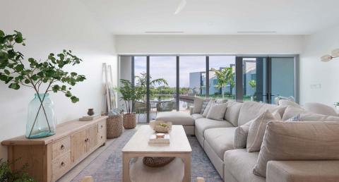 This image shows a stylish and contemporary living room with a serene waterfront view through large floor-to-ceiling windows