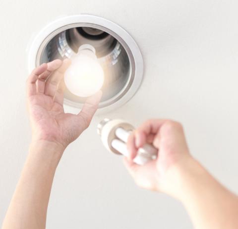 The image shows a person changing a light bulb in a ceiling light fixture