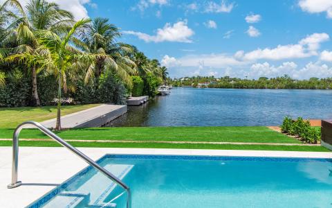 The image displays an upscale outdoor setting featuring a bright blue swimming pool at the forefront with a stainless steel ladder on its side
