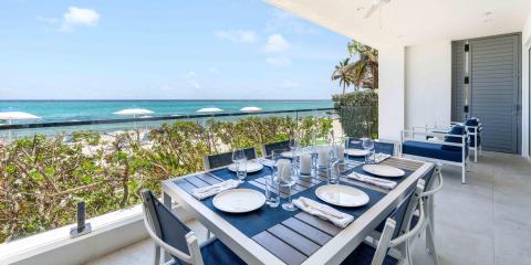 This image shows a beautifully arranged outdoor dining area on a balcony overlooking a beach