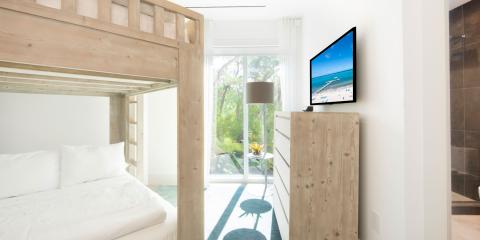 The image shows a modern and bright bedroom with a large window that provides a view of lush greenery outside