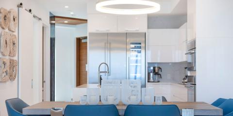 The image depicts a modern kitchen interior, featuring a sleek design with a neutral color palette accented by blue chairs