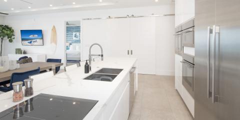 The image shows a modern kitchen that opens to a dining area and a glimpse into a bedroom