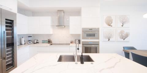 This image shows a modern, stylish kitchen featuring clean white cabinetry with flush doors and marble countertops