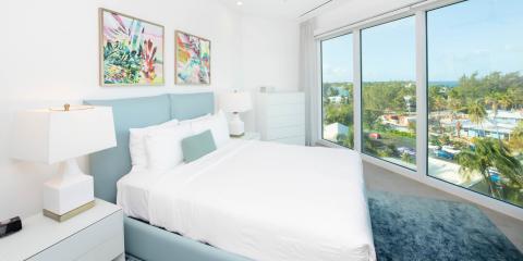 The image shows a bright, modern bedroom with a large window offering a beautiful view over a tropical landscape