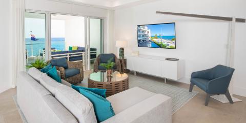 The image depicts a modern, well-lit living room with a view of a beachfront
