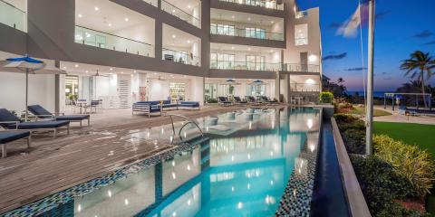 This image shows a luxurious outdoor pool area of a modern beachfront building during the evening