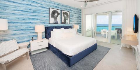 The image shows a modern, well-furnished bedroom overlooking a seaside view