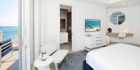This image shows a modern and well-lit hotel or apartment bedroom with a striking view of the sea