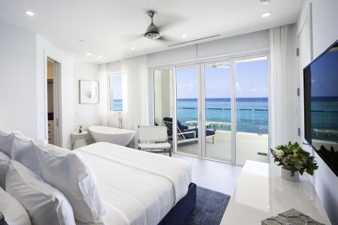 This image shows a modern, luxurious bedroom with an oceanfront view