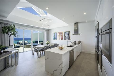 The image shows a luxurious, modern kitchen and living area with a beautiful ocean view