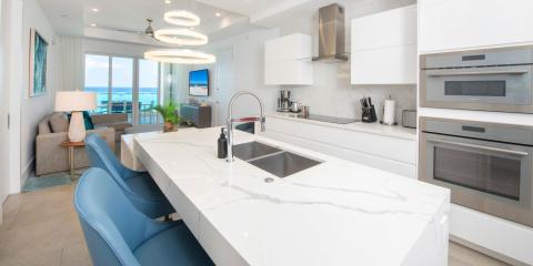 This image shows a modern, brightly lit kitchen that opens up to a spacious living area with a beautiful ocean view through large glass doors