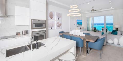 This image shows a modern, luxurious kitchen and dining area which seamlessly opens onto a living room with a stunning view of the ocean
