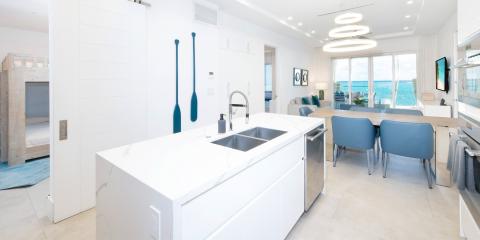 This image shows a modern, luxurious kitchen that flows into a dining and living area, with a stunning ocean view through large glass windows