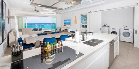 The image shows a modern and luxurious interior space that seamlessly blends a kitchen, living area, and dining space with an extraordinary ocean view