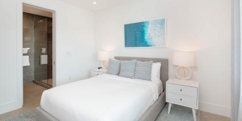 This is an image of a modern bedroom featuring a neatly made bed with a gray upholstered headboard, complemented by several pillows in varying patterns of blue and white stripes