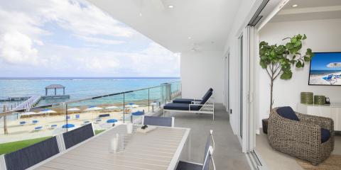 The image displays a luxurious coastal balcony and interior setting, likely part of a modern beachfront property