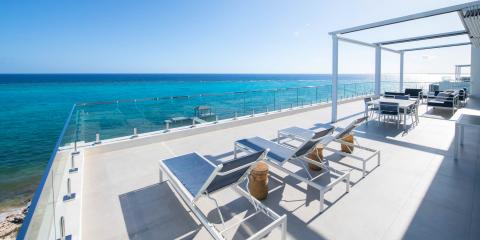 The image displays a modern, luxurious outdoor terrace overlooking a vibrant blue sea