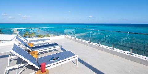 The image features a luxurious oceanfront terrace with a stunning view of a turquoise ocean