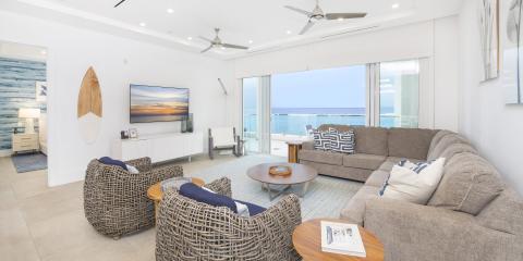 The image features a modern beachfront living room with a bright, airy atmosphere