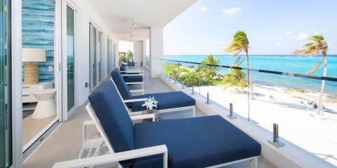 The image shows a beautiful, scenic view from a coastal balcony overlooking a sandy beach and clear blue waters