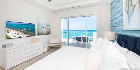 The image shows a luxurious, modern bedroom with a direct view of the beach and ocean