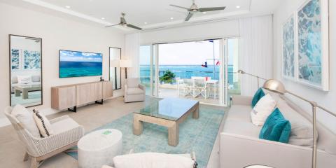 The image shows a modern and bright living room that opens up to a beautiful beachfront view