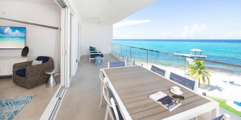 This image depicts a luxurious beachfront balcony overlooking a stunning crystal-clear ocean