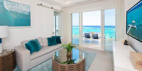 This image depicts a modern, stylish beachfront living room that opens to a balcony overlooking a stunning ocean view