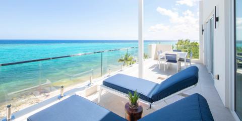 This image features a luxurious beachfront balcony overlooking a clear, turquoise ocean