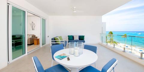 This image shows a bright and airy balcony with a picturesque view of a beach and the ocean