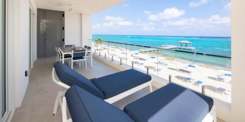 This image shows a luxurious beachfront balcony overlooking a sandy beach with crystal-clear turquoise water
