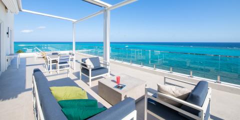 This image shows a luxurious oceanfront terrace with a stunning view of a vibrant turquoise sea