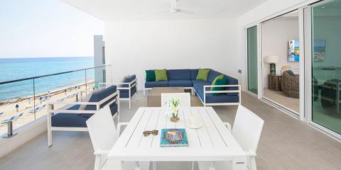 This image shows a modern, stylishly decorated outdoor terrace or balcony that overlooks a beautiful beach
