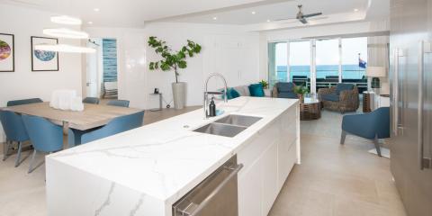 This image shows a spacious, modern kitchen and living area with a stunning ocean view