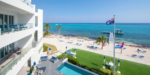This image features a luxurious beachfront property with a modern multi-story accommodation building that overlooks a beautiful sandy beach and clear blue waters