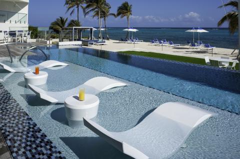 This image shows a luxurious outdoor setting that features a swimming pool with uniquely designed lounge chairs partially submerged in the water