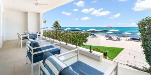 This image shows a stylish seaside terrace, designed for outdoor dining and relaxation, overlooking a beautiful beach