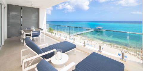 The image shows a beautiful oceanfront balcony overlooking a stunning beach with clear turquoise waters