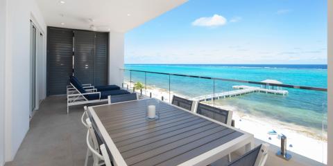 The image shows a scenic view from a beachfront balcony overlooking a clear blue ocean